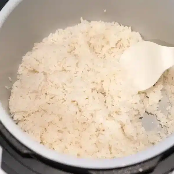 A pot of fluffy white rice fills most of the Ninja Foodi, with a white plastic spatula resting on the side.