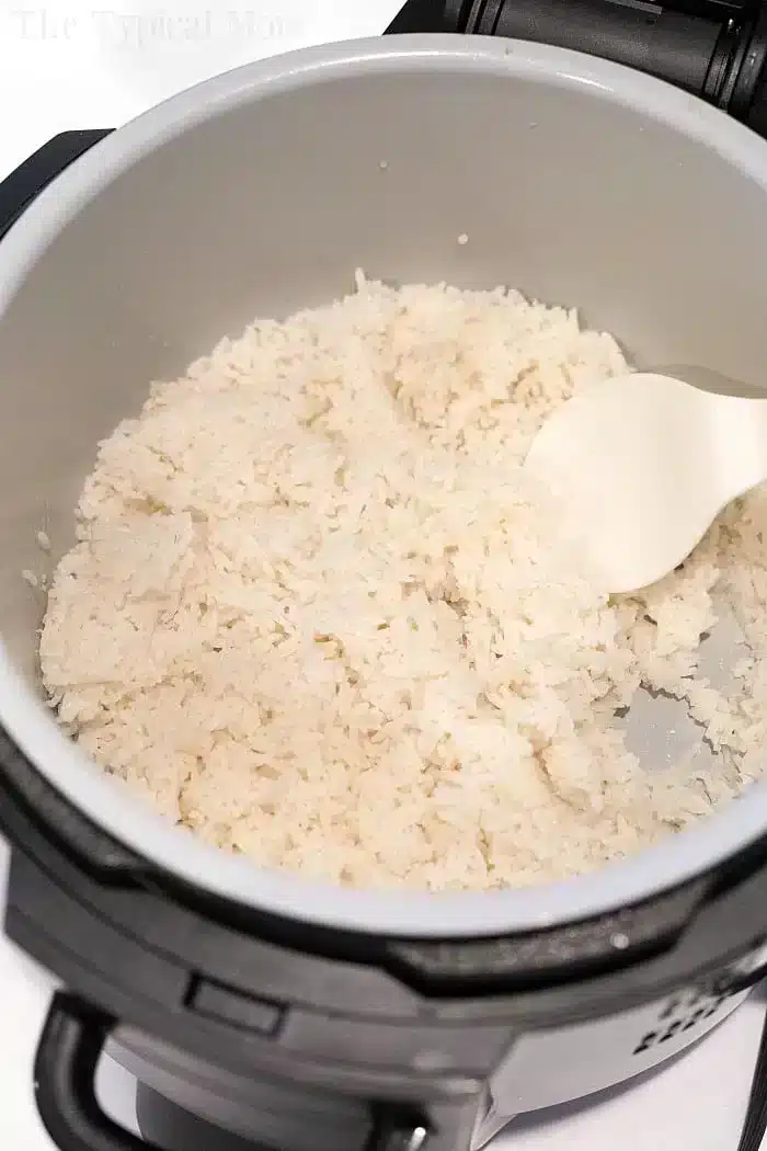 A pot of fluffy white rice fills most of the Ninja Foodi, with a white plastic spatula resting on the side.