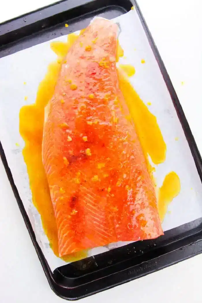 A marinated piece of raw salmon, placed on a baking sheet lined with parchment paper