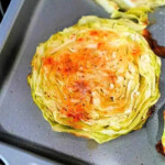 Baked cabbage steaks rest on a baking tray, perfectly seasoned with spices and boasting deliciously browned edges.