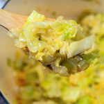 A wooden spoon holding stewed cabbage above a pot filled with more tender, cooked cabbage.