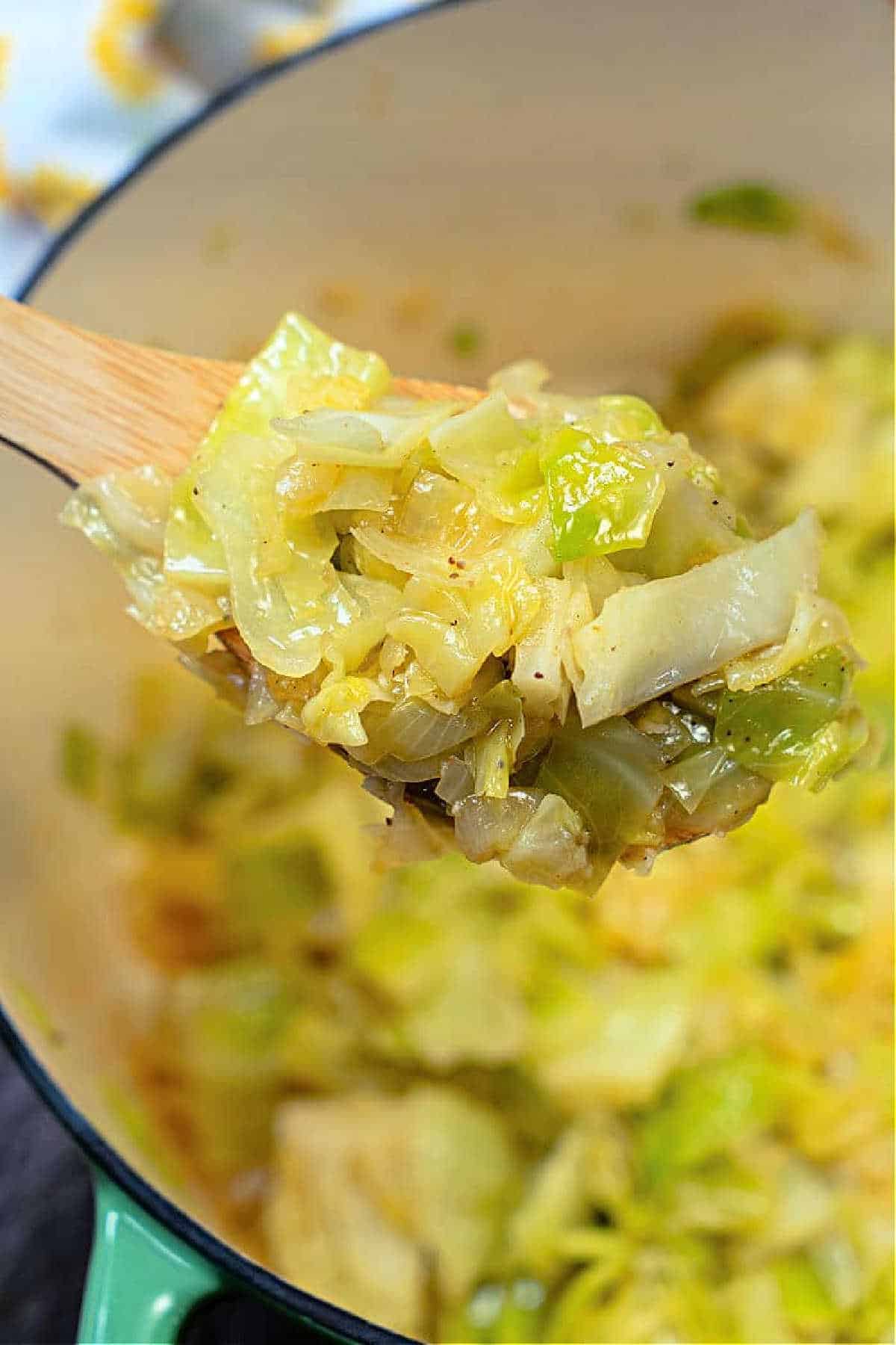 A wooden spoon holding stewed cabbage above a pot filled with more tender, cooked cabbage.