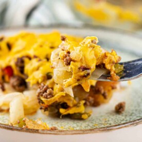 Fork with cheesy hamburger casserole, featuring ground beef, cheese, vegetables, and a hint of cabbage on a plate.