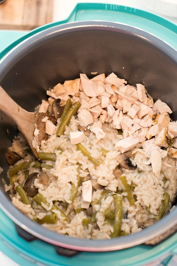 Rice with green beans, mushrooms, and tender chicken pieces in a pressure cooker, stirred with a wooden spoon.