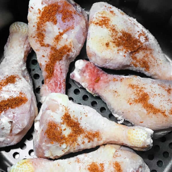 Six raw, seasoned chicken drumsticks, perfect for making Frozen Chicken Legs in Air Fryer, are placed in the basket and ready to be cooked.