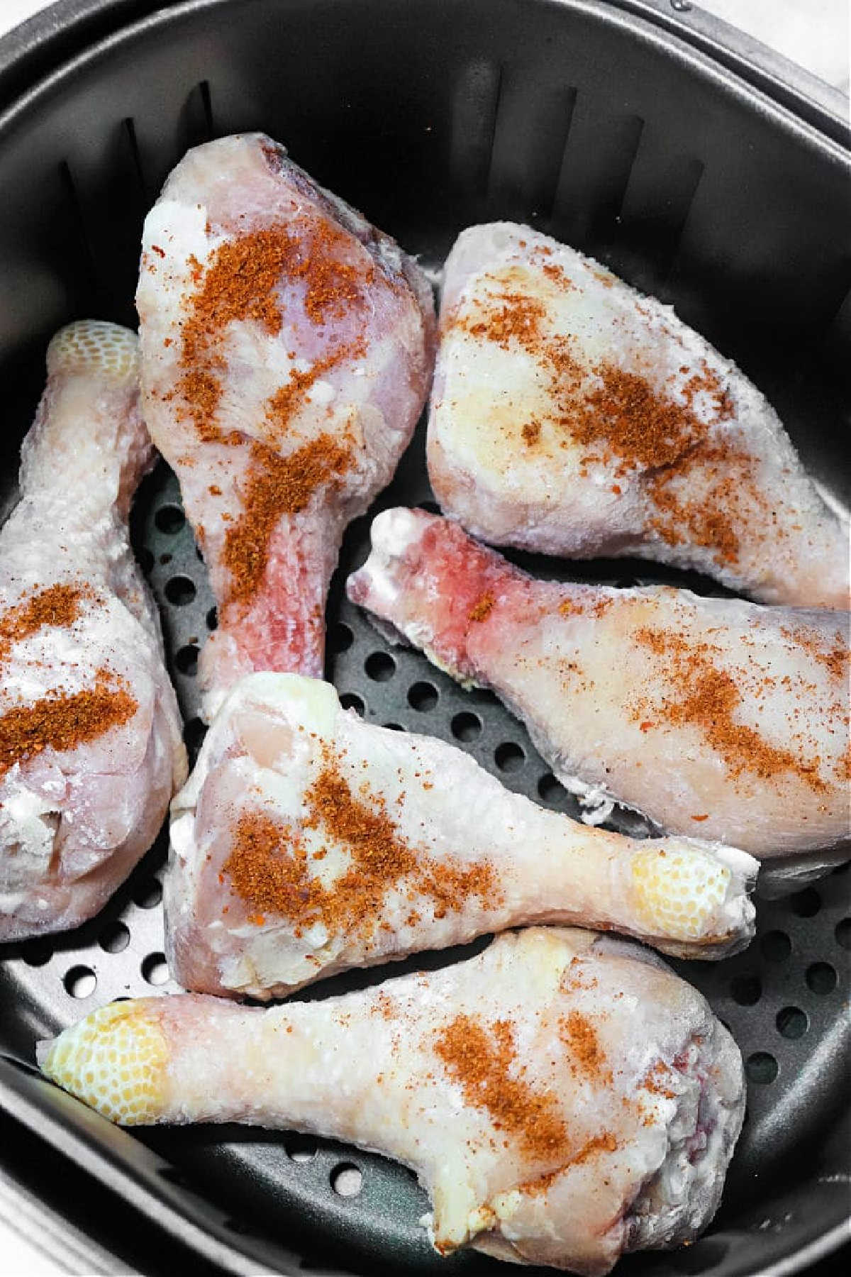Six raw, seasoned chicken drumsticks, perfect for making Frozen Chicken Legs in Air Fryer, are placed in the basket and ready to be cooked.