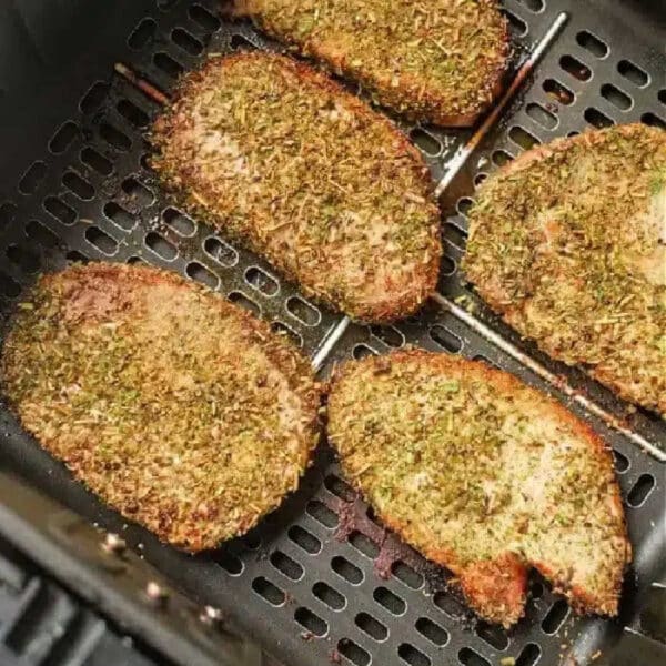 Seasoned pork chops, or pork steak in air fryer, cook to golden brown perfection, evenly spaced in the basket.