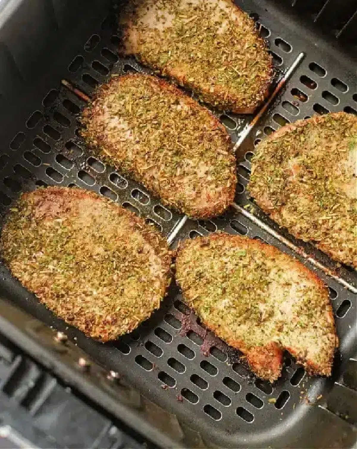 Seasoned pork chops, or pork steak in air fryer, cook to golden brown perfection, evenly spaced in the basket.
