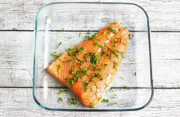 A raw salmon fillet, seasoned with chopped herbs.