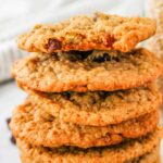 A stack of steel cut oatmeal raisin cookies proudly sits on a white surface, with a jar of steel cut oats in the background.