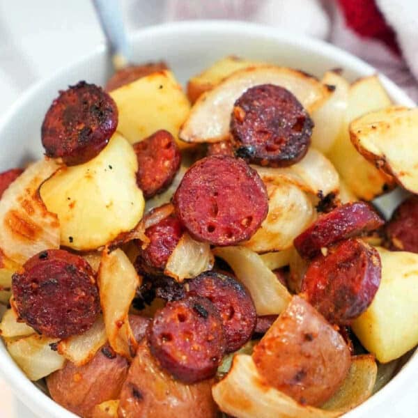 A bowl of roasted potatoes, onions, and sliced air fryer sausage, cooked and lightly browned.