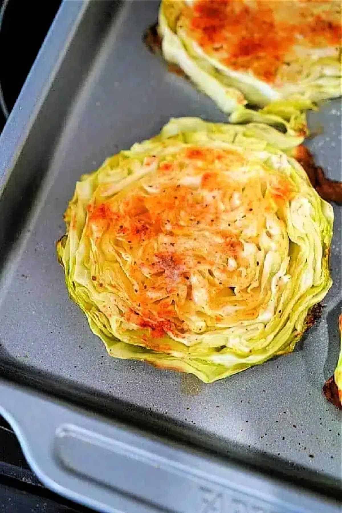Baked cabbage steaks sliced into rounds on a baking sheet, seasoned with herbs and spices.