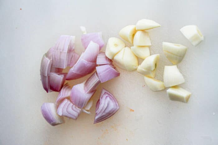 Chopped pieces of red onions and garlic cloves are arranged on a white cutting board. The red onion pieces are on the left, and the garlic pieces, key ingredients for a Garlic Chili Paste Recipe, are on the right.