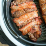 A cooked air fryer steak wrapped in crispy bacon sits in the basket, ready to be served.