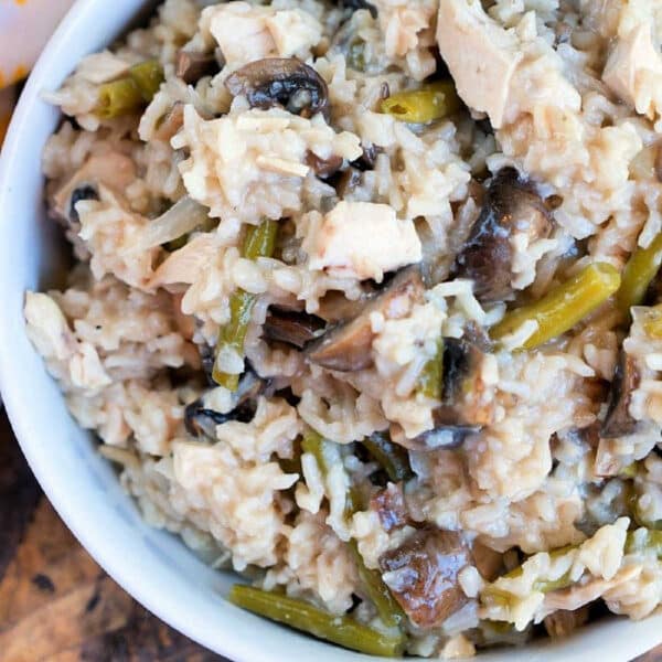 A close-up of a bowl filled with creamy chicken mushroom rice casserole, featuring tender chicken, mushrooms, rice, and vibrant green beans.