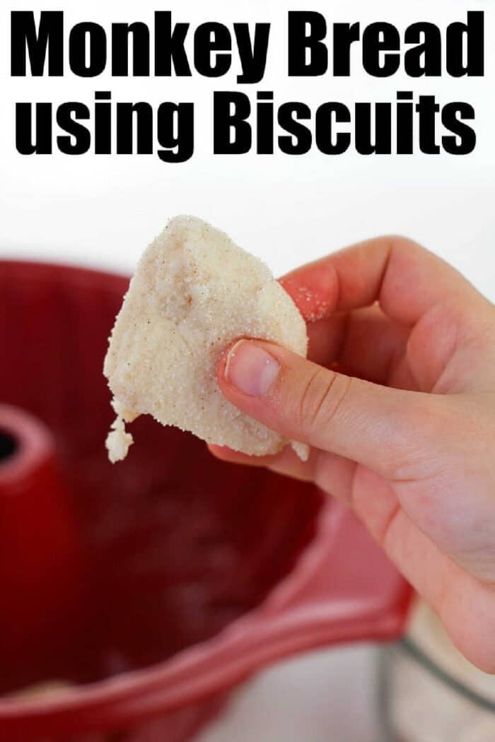 A hand holds a sugar-coated biscuit in front of a red bundt pan; text reads Easy Monkey Bread Recipe using Biscuits.