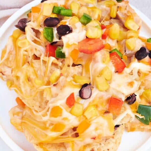 A plate of cheesy ninja foodi Nachos topped with black beans, corn, diced bell peppers, and jalapeños.