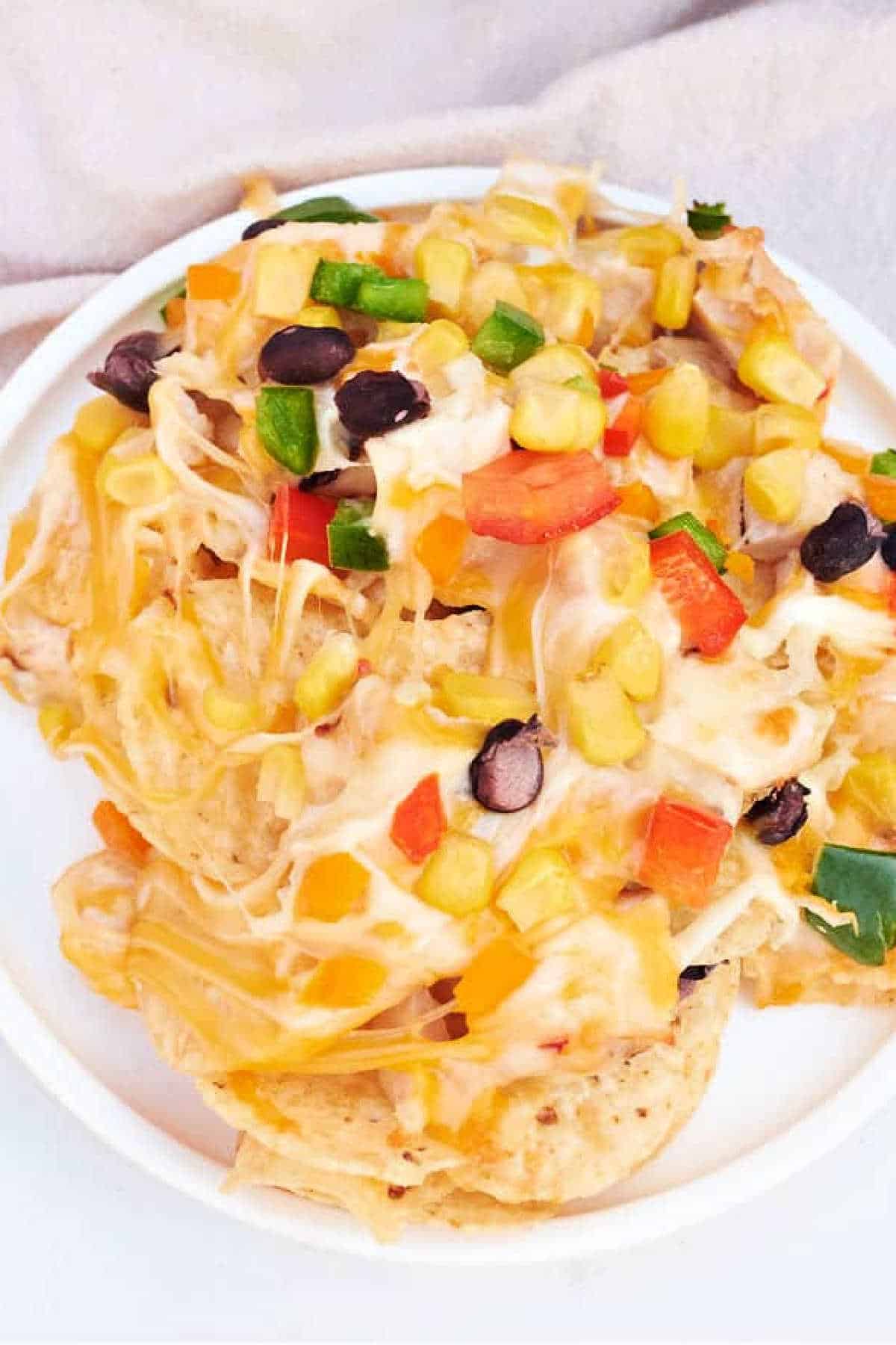 A plate of cheesy ninja foodi Nachos topped with black beans, corn, diced bell peppers, and jalapeños.