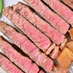 A plate with several slices of medium-rare beef strip loin steaks arranged in a line. The meat is pink in the center with a browned outer edge, featuring a juicy texture. Some greens are visible in the corner of the plate, showing you how to cook beef strip loin steaks to perfection.