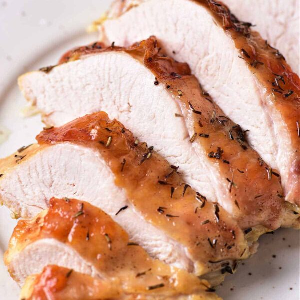 A close-up of several slices of cooked turkey breast confit on a white plate. The turkey has a crispy, browned skin with herbs visible on the surface. The inside appears tender and juicy.