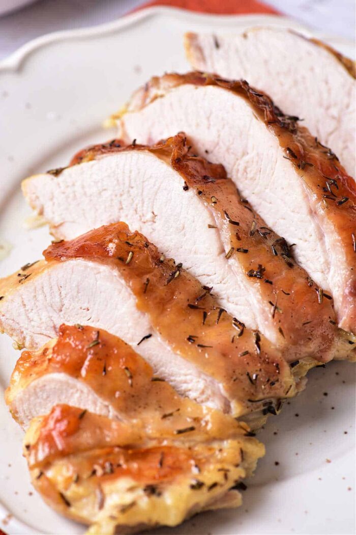 Sliced roasted turkey confit breast with a crispy, seasoned skin on a white plate. The meat appears moist and tender, with visible seasonings on the golden-brown crust.