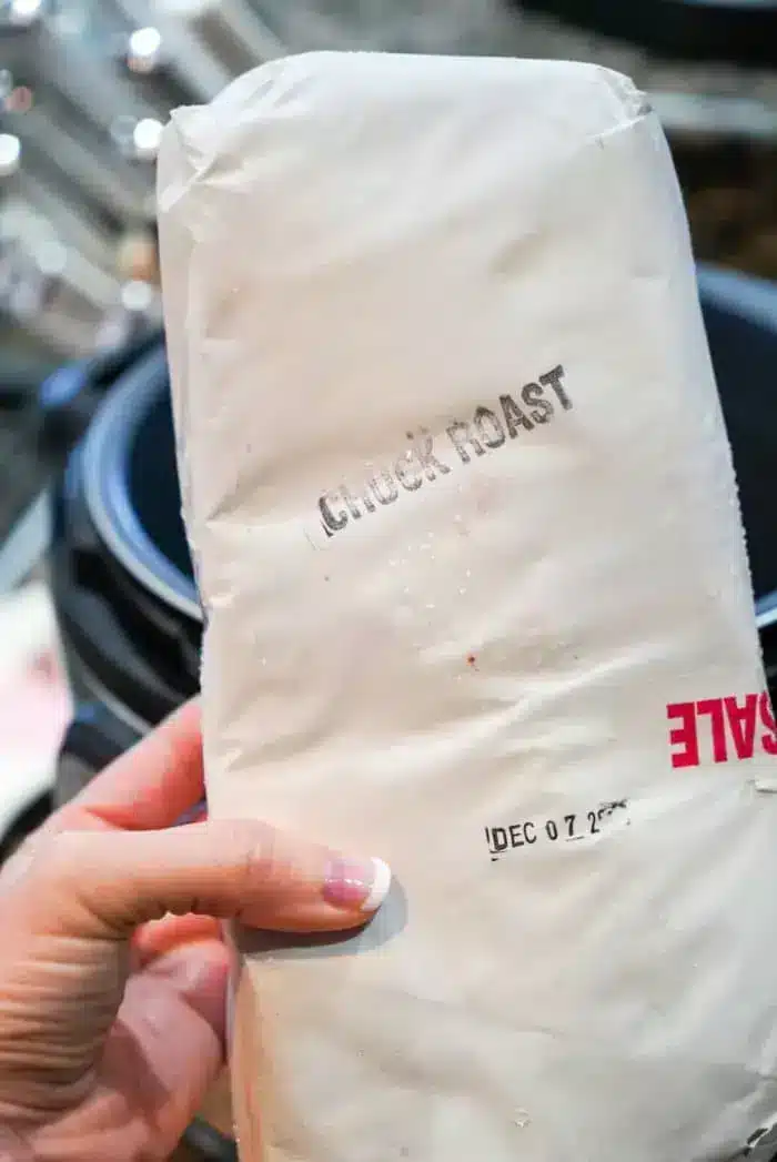 A hand holds a wrapped package labeled "Chuck Roast," ideal for the slow cooker, with a visible sale sticker and a date marked "DEC 07 2023.