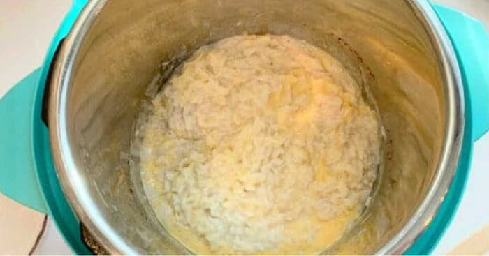 Cooked pressure cooker coconut rice pudding inside a teal-handled pot, creamy and slightly clumped around the edges.