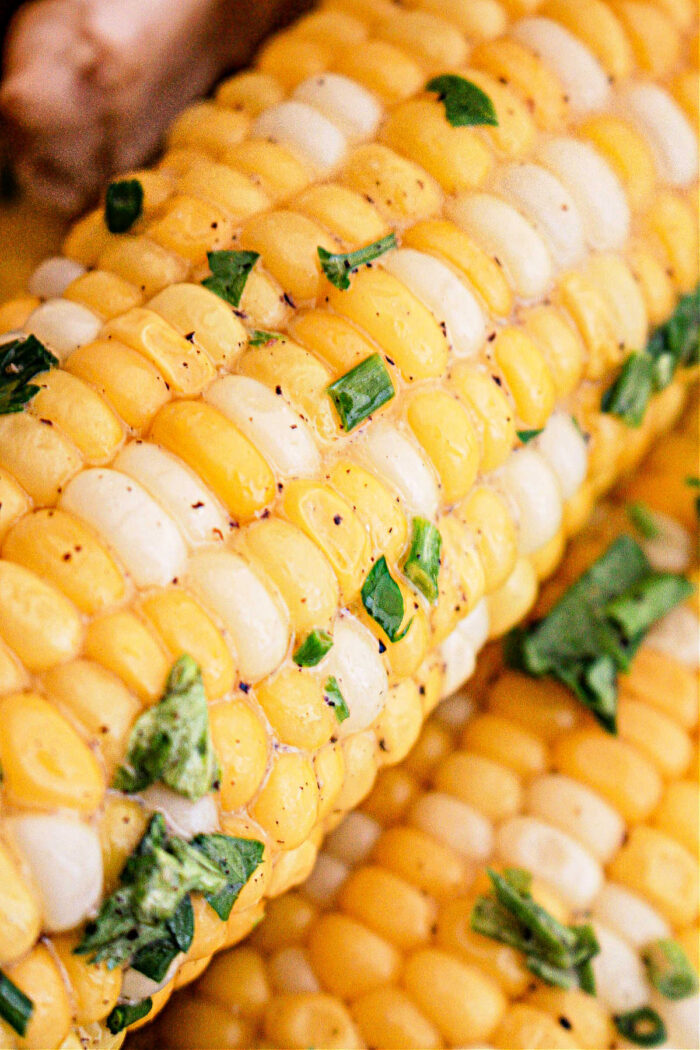 Close-up image of Crockpot Corn on the Cob sprinkled with fresh chopped parsley or cilantro. The corn kernels are alternating yellow and white, showcasing a vibrant and delicious dish.