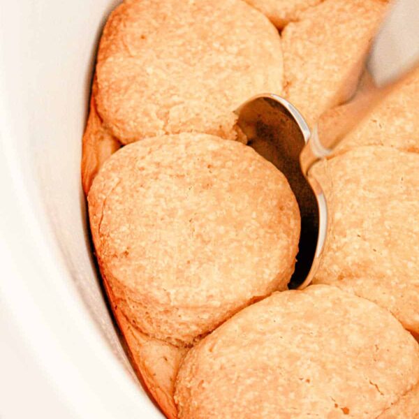 Slow Cooker Biscuits and Gravy. There is a silver spoon resting on top of one of the golden brown biscuits. The biscuits are arranged close together in the dish.