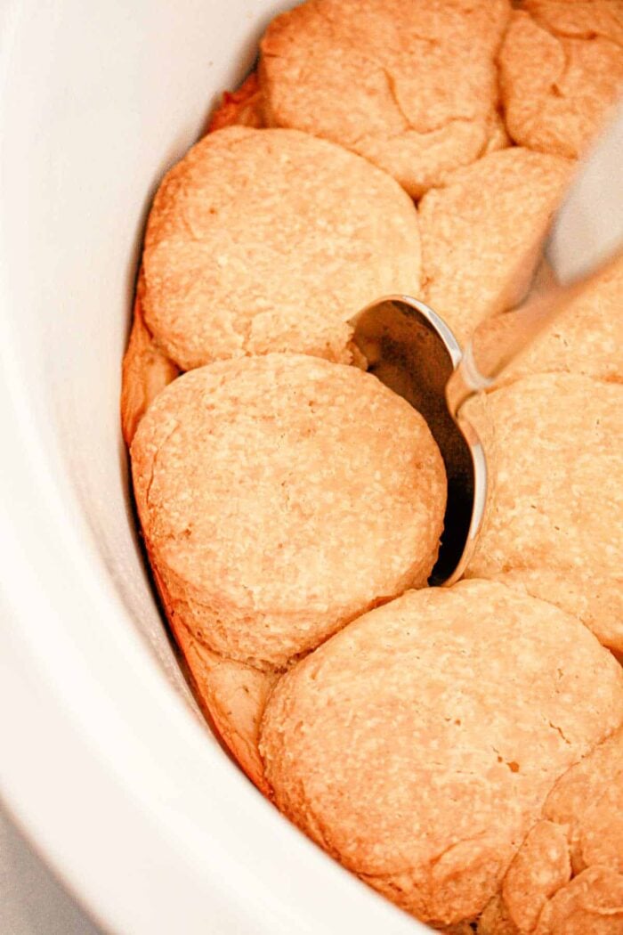 Slow Cooker Biscuits and Gravy. There is a silver spoon resting on top of one of the golden brown biscuits. The biscuits are arranged close together in the dish.