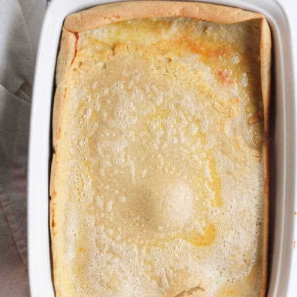 Golden-brown Dutch baby pancake, baked to perfection as one of the best pancakes in the oven, sits in a white baking dish on a cooling rack.