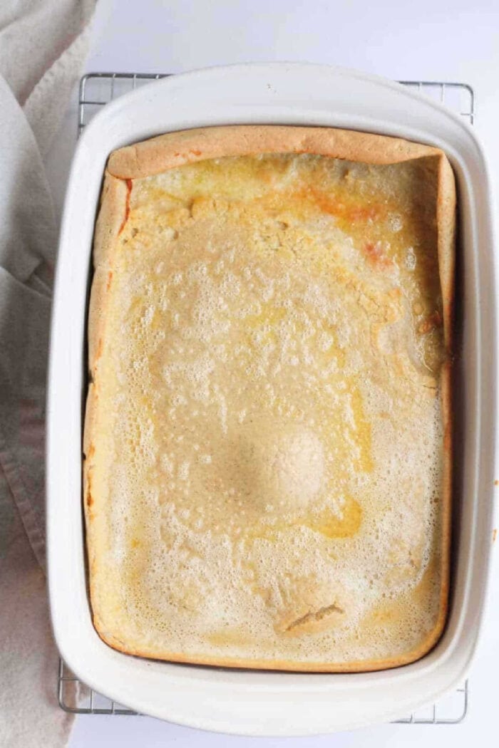Golden-brown Dutch baby pancake, baked to perfection as one of the best pancakes in the oven, sits in a white baking dish on a cooling rack.