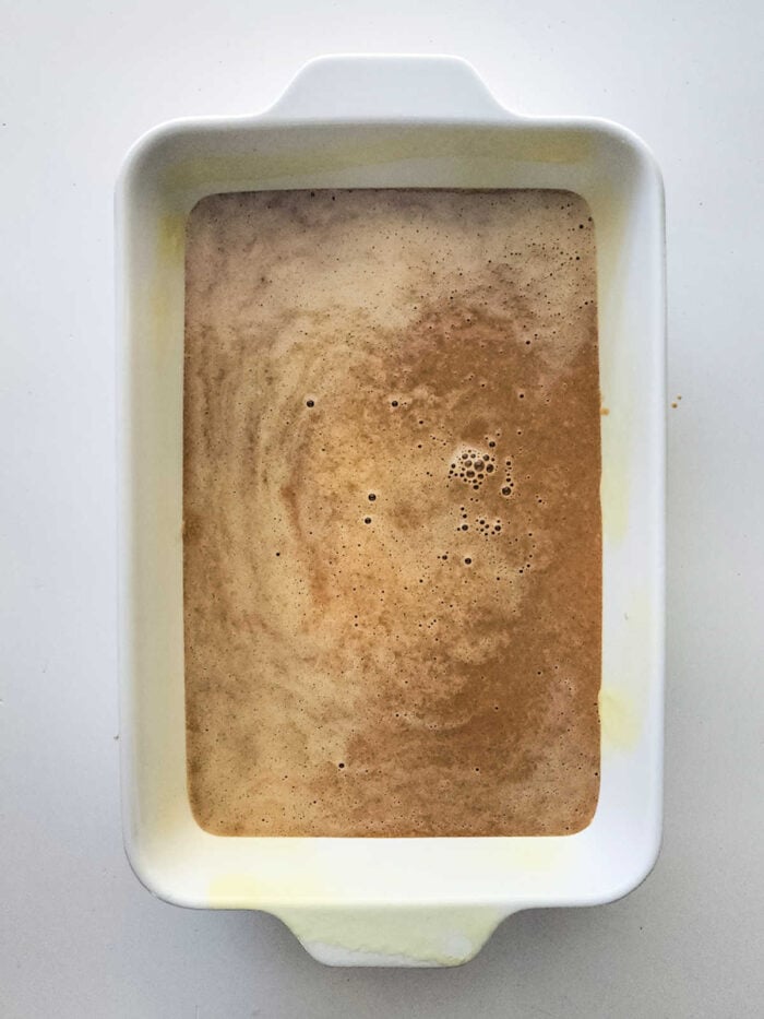 A white baking dish filled with a light brown, frothy Sweet Potato Dump Cake batter rests on a white surface.