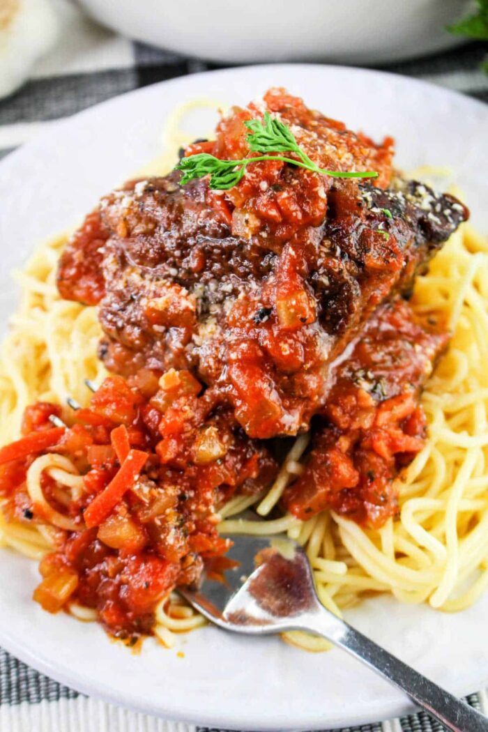 A plate of spaghetti topped with a hearty portion of meat sauce garnished with herbs sits invitingly on a checkered cloth. A fork rests on the edge, ready for use, reminiscent of the anticipation before savoring delicious short rib tacos.