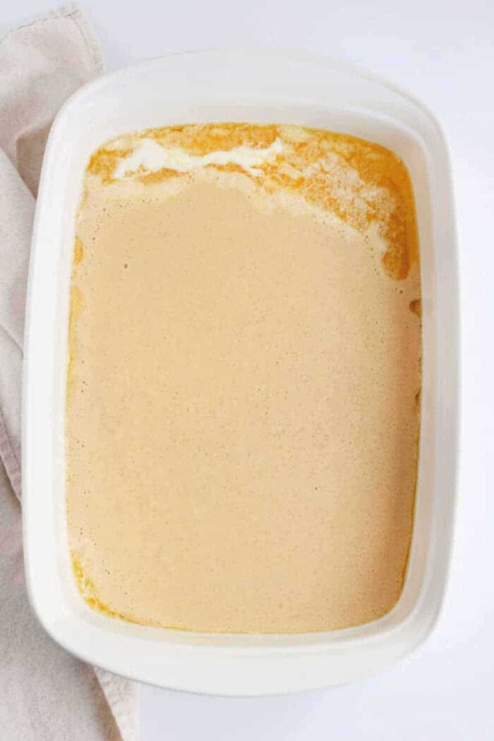 A white baking dish filled with a creamy, light brown liquid mixture, partially set around the edges—perfect for making fluffy Pancakes in the Oven.