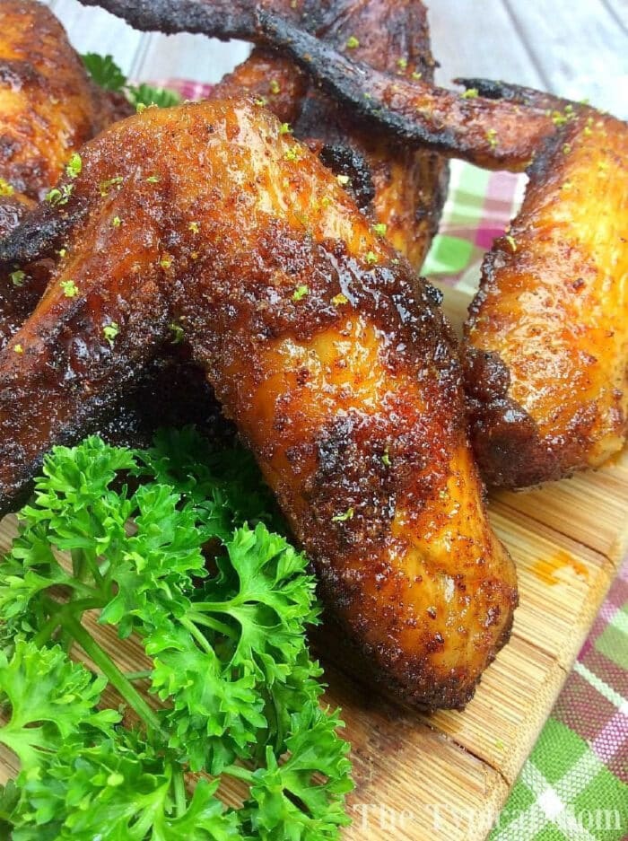 Close-up of seasoned, crispy baked Ninja Foodi chicken wings on a wooden board, garnished with fresh parsley.