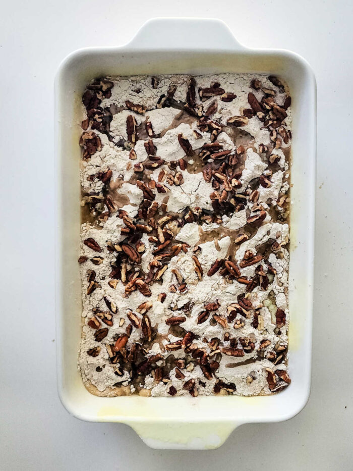Rectangular baking dish with flour mixture and chopped pecans on top, ready to be baked into a delicious Sweet Potato Dump Cake.