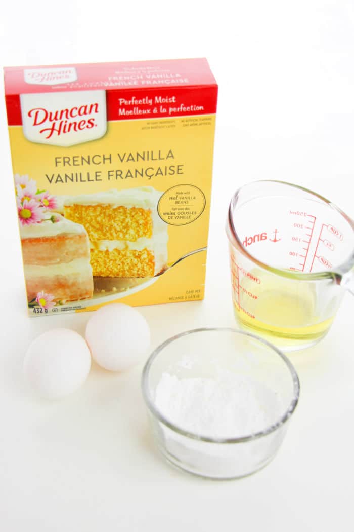 Box of French vanilla cake mix, two eggs, a measuring cup with egg whites, and a bowl of powdered sugar—everything you need for quick and delicious 3 Ingredient Cake Mix Cookies.