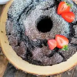 A delicious family meal, this chocolate bundt cake topped with powdered sugar and garnished with sliced strawberries sits beautifully on a wooden board.