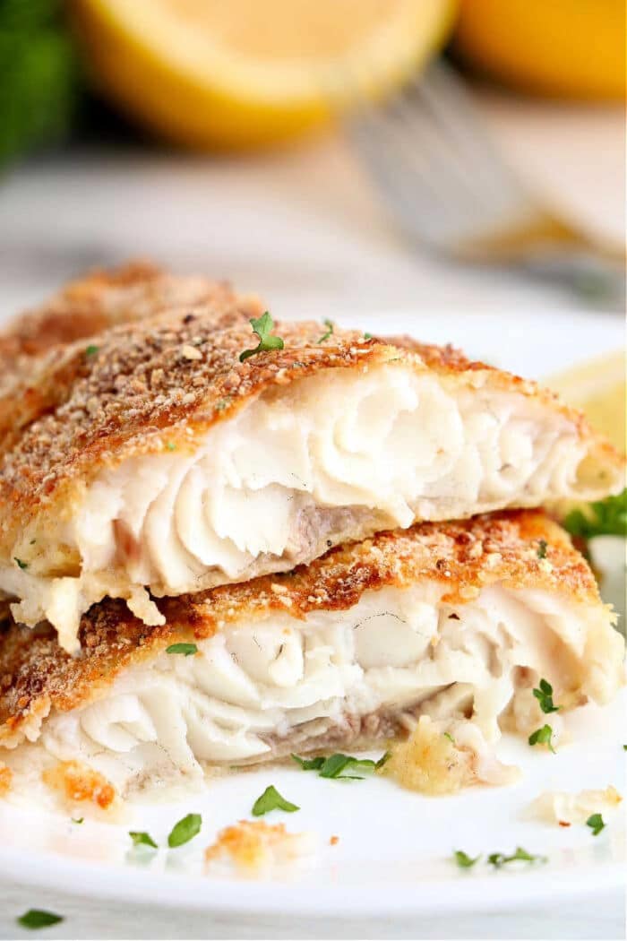 Two crispy, golden-brown air fryer catfish fillets stacked on a plate, garnished with chopped herbs.