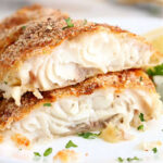 Two pieces of baked, breaded white fish fillets—similar to air fryer catfish—garnished with chopped parsley on a white plate.