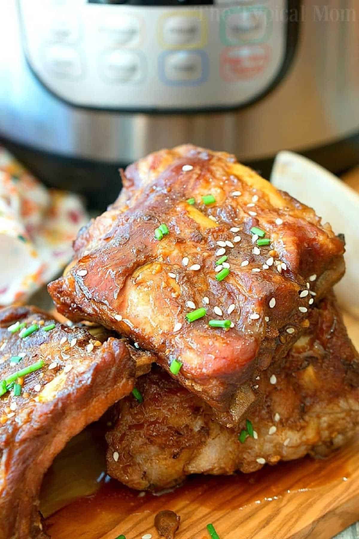 Instant Pot teriyaki ribs recipe are sweet and spicy all rolled into one. Fall off the bone pressure cooker ribs done in 25 minutes and just amazing! If you love beef or pork ribs but don't have all day to make them perfect use this method, you'll never make ribs another way again. #instantpot #ribs #teriyaki #pressurecooker #pork #beef #dinner #crockpotexpress #instantpotrecipes #thetypicalmom #ninjafoodi A stack of glazed pork ribs garnished with chives and sesame seeds sits temptingly in front of an Instant Pot, showcasing a mouthwatering instant pot teriyaki ribs recipe.