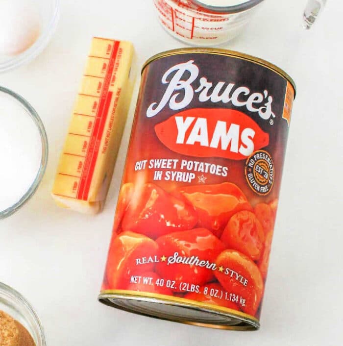 A can of Bruce’s Yams, labeled "Cut Sweet Potatoes in Syrup" and "Real Southern Style," perfect for a Recipe for Sweet Potato Pie with Sweetened Condensed Milk. The can is 40 ounces (2 lbs 8 oz / 1.134 kg). Nearby are a stick of butter, a measuring cup, and other cooking ingredients.