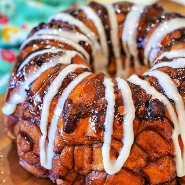 A glazed Rhodes monkey bread ring drizzled with white icing, sitting on a wooden surface.