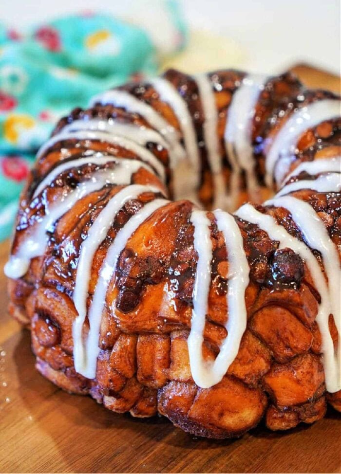 A glazed Rhodes monkey bread ring drizzled with white icing, sitting on a wooden surface.