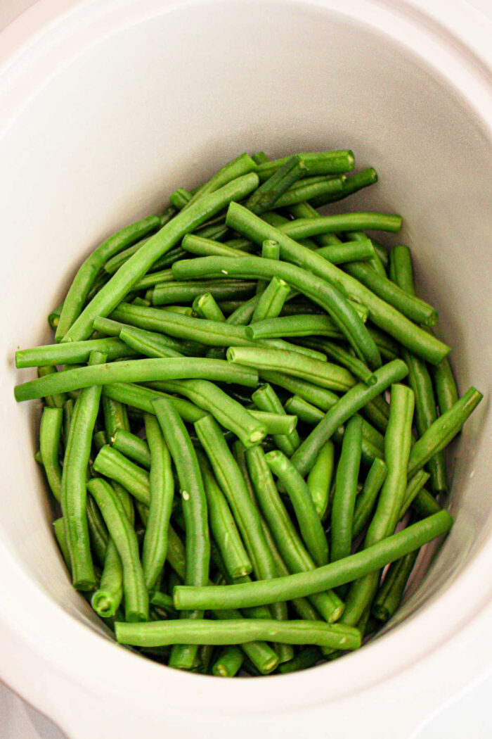 A ceramic bowl is filled with a pile of raw green beans, freshly cut and vibrant in color, waiting to be prepared or added to your crockpot for a delicious meal.