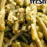 Close-up image of cooked green beans labeled "Crockpot Green Beans Recipe." The green beans are garnished with chopped garlic and herbs, and displayed on a white plate with some cooking liquid visible.