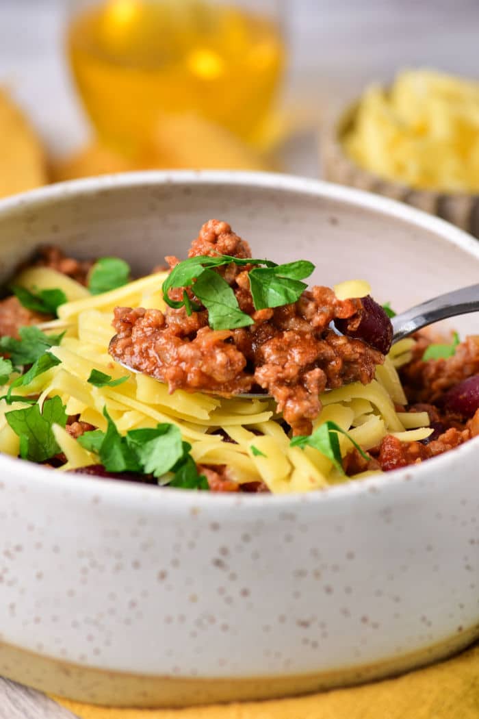 A bowl of Dutch Oven Chili topped with shredded cheese and fresh parsley, with a spoonful lifted above the bowl.