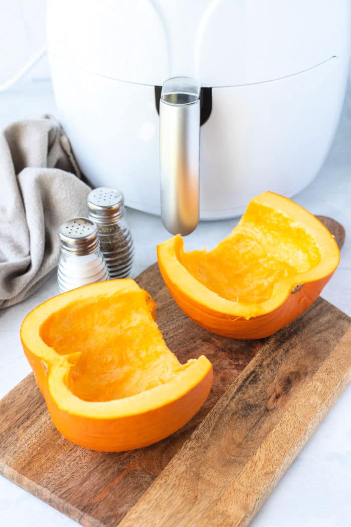 Two pumpkin halves rest on a wooden cutting board beside salt and pepper shakers, ready to be transformed into delicious air fryer pumpkin.