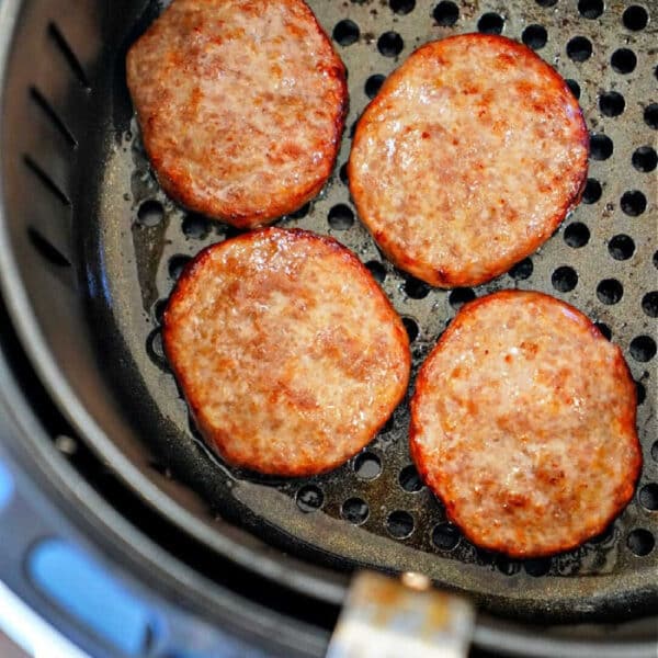Four cooked sausage patties in an air fryer basket, showing just how easy it is to make delicious sausage patties in air fryer for a quick breakfast.